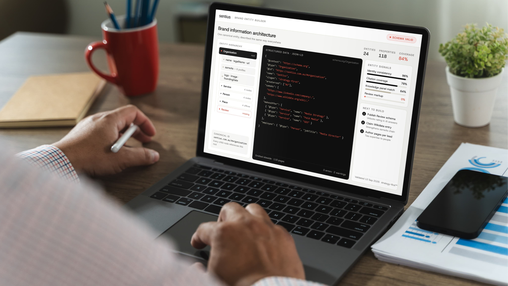 Laptop showing a brand entity builder tool with structured JSON-LD data, entity hierarchy, and schema validation status